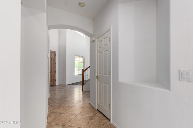 hall with light tile patterned floors, arched walkways, baseboards, and stairs