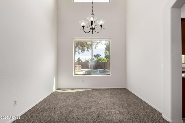 empty room with a high ceiling, a chandelier, baseboards, and carpet