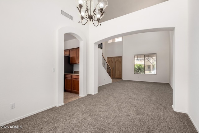 empty room with visible vents, stairs, light colored carpet, arched walkways, and a notable chandelier