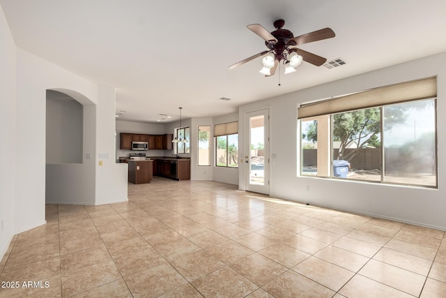 unfurnished living room featuring arched walkways, a wealth of natural light, ceiling fan, and visible vents