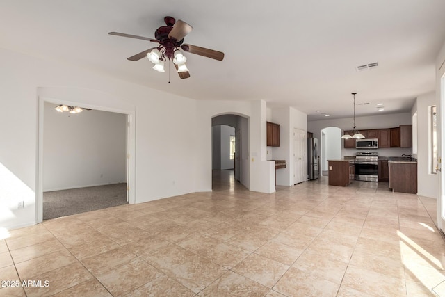 unfurnished living room with light tile patterned floors, arched walkways, ceiling fan, and visible vents
