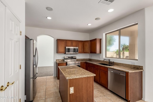 kitchen featuring visible vents, a kitchen island, arched walkways, a sink, and stainless steel appliances