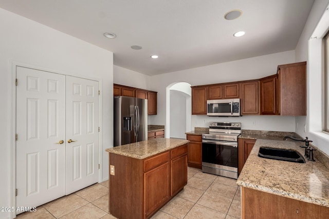 kitchen featuring a kitchen island, appliances with stainless steel finishes, arched walkways, a sink, and light tile patterned floors