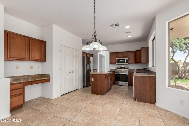 kitchen featuring appliances with stainless steel finishes, a sink, built in desk, a kitchen island, and visible vents
