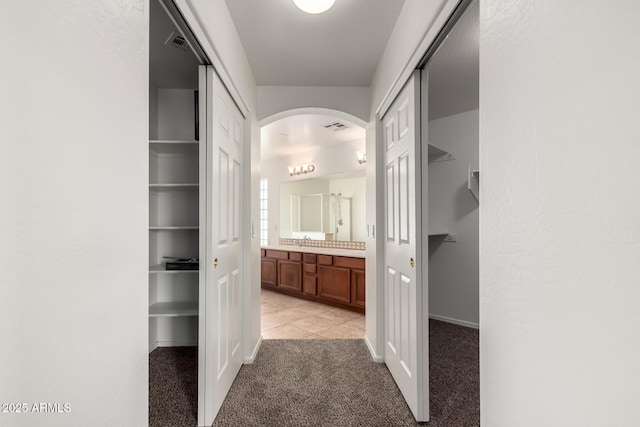corridor featuring arched walkways, baseboards, visible vents, and light carpet