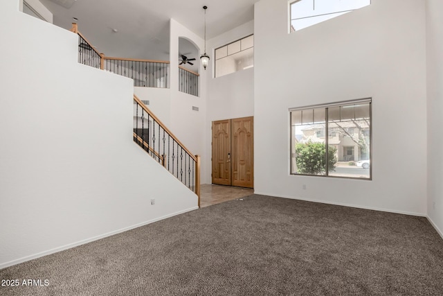 unfurnished living room with a ceiling fan, carpet floors, baseboards, a high ceiling, and stairs