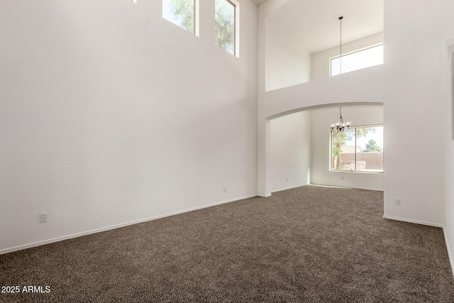 carpeted empty room featuring baseboards, a high ceiling, and a notable chandelier