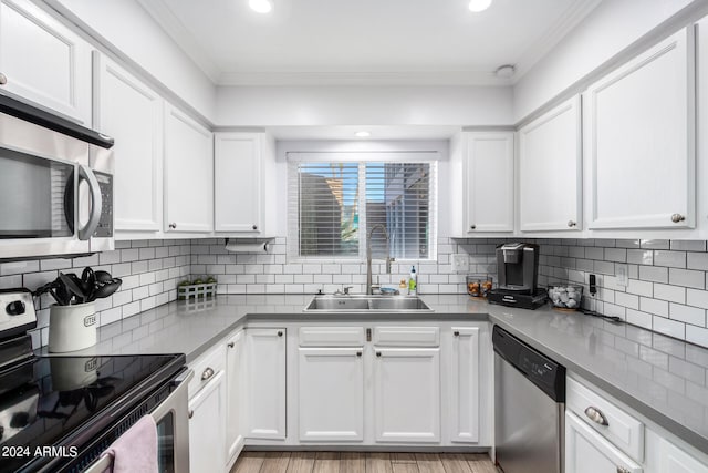 kitchen featuring light wood-type flooring, ornamental molding, white cabinetry, sink, and appliances with stainless steel finishes