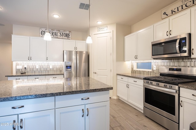 kitchen featuring pendant lighting, white cabinets, tasteful backsplash, dark stone countertops, and stainless steel appliances