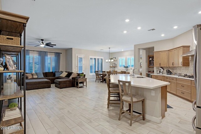 kitchen with sink, decorative backsplash, an island with sink, ceiling fan with notable chandelier, and a breakfast bar area