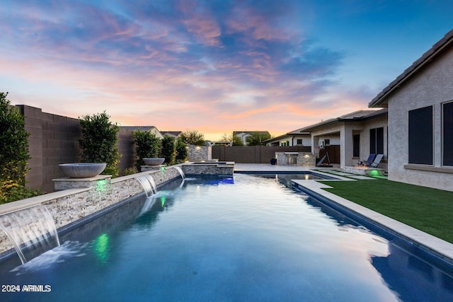 pool at dusk with a patio and pool water feature