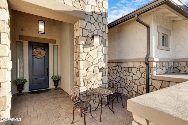 entrance to property with stucco siding, stone siding, and a patio area