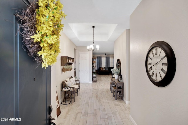 hall featuring a tray ceiling, baseboards, light wood-style floors, and a chandelier