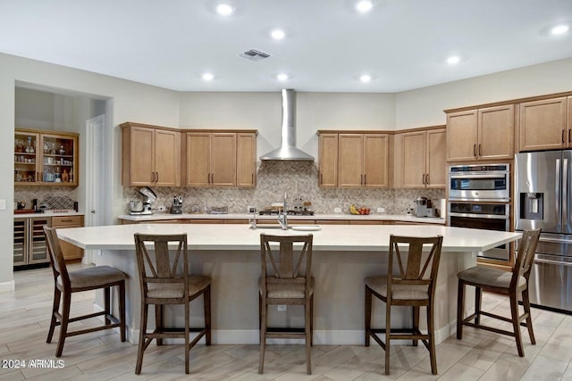 kitchen featuring visible vents, light countertops, a large island with sink, appliances with stainless steel finishes, and wall chimney exhaust hood