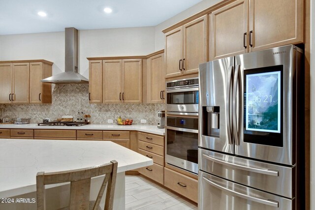 kitchen featuring wall chimney range hood, backsplash, appliances with stainless steel finishes, and light stone counters