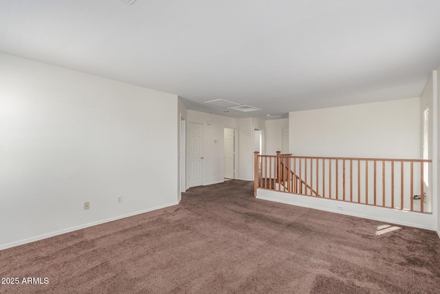 carpeted spare room featuring attic access and baseboards