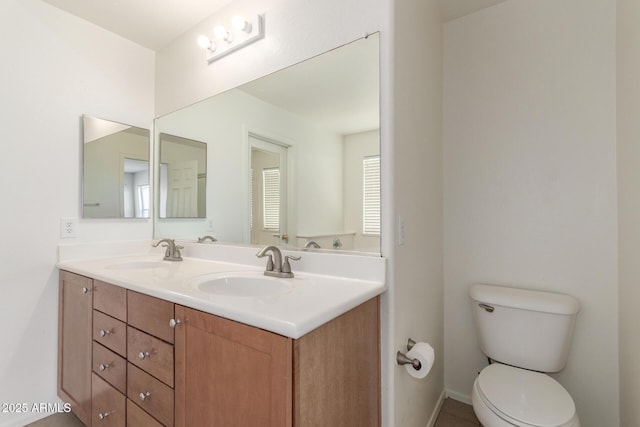 full bath with baseboards, a sink, toilet, and double vanity