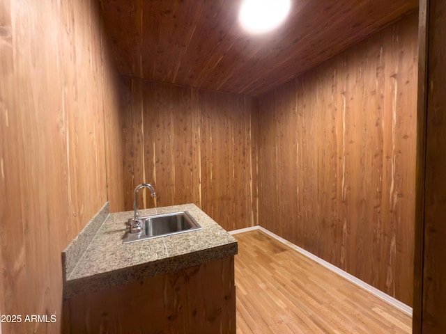 interior space featuring wooden ceiling, light hardwood / wood-style floors, sink, and wood walls