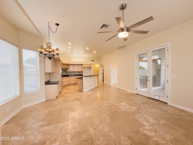 kitchen with hanging light fixtures, ceiling fan with notable chandelier, sink, and a center island with sink