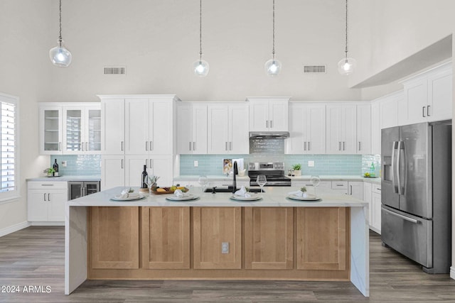 kitchen featuring appliances with stainless steel finishes, an island with sink, white cabinetry, and a towering ceiling