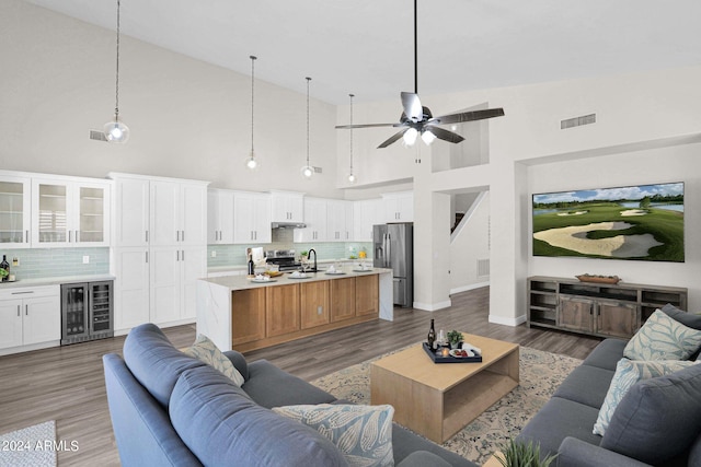 living room with beverage cooler, ceiling fan, hardwood / wood-style flooring, high vaulted ceiling, and sink