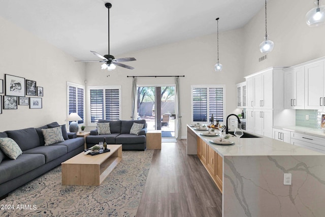 living room with ceiling fan, high vaulted ceiling, sink, and light wood-type flooring