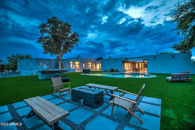 patio terrace at dusk with a yard, an outdoor pool, a fire pit, and grilling area