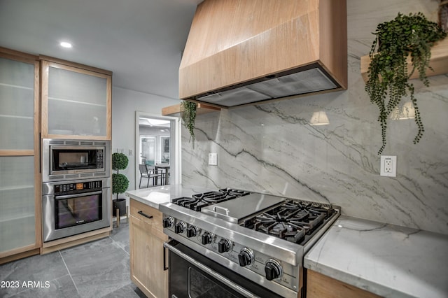 kitchen with light stone counters, light brown cabinets, appliances with stainless steel finishes, tasteful backsplash, and custom range hood