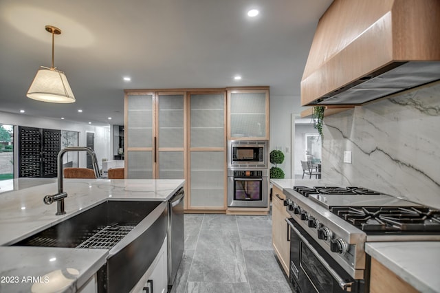 kitchen with stainless steel appliances, a sink, wall chimney range hood, light stone countertops, and tasteful backsplash