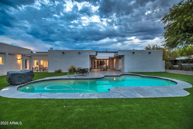 pool at dusk featuring an outdoor pool, a patio area, and a lawn