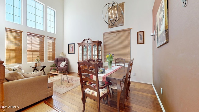 dining area featuring wood-type flooring, a chandelier, and a high ceiling