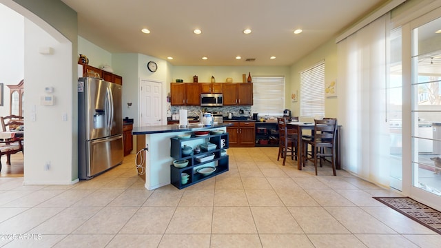 kitchen featuring stainless steel appliances, light tile patterned flooring, a center island, and a kitchen bar