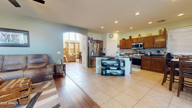 kitchen featuring appliances with stainless steel finishes, tasteful backsplash, a center island, light tile patterned floors, and ceiling fan