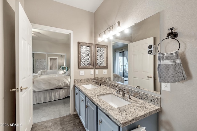 ensuite bathroom with a textured wall, a sink, ensuite bath, and double vanity