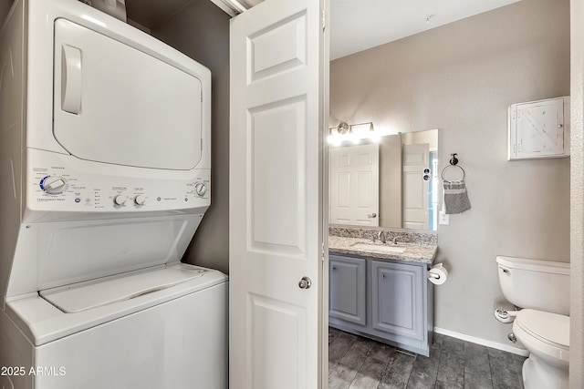 clothes washing area featuring laundry area, wood finish floors, stacked washer / dryer, a sink, and baseboards