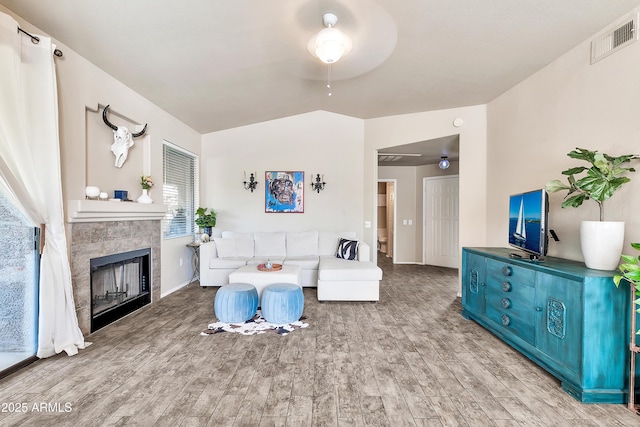 living area featuring a tile fireplace, visible vents, vaulted ceiling, and wood finished floors