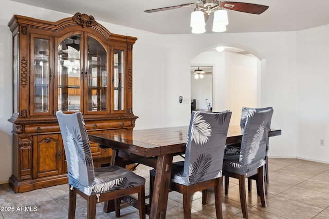 dining space with light tile patterned flooring, arched walkways, ceiling fan, and baseboards
