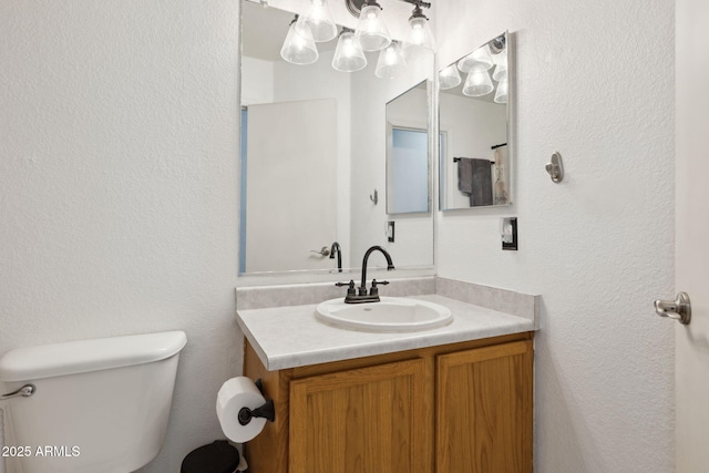 bathroom with toilet, vanity, and a textured wall