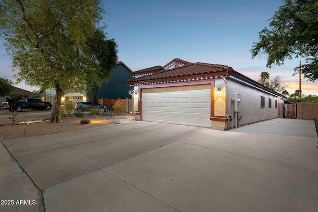 view of front of house with a tiled roof, fence, a garage, and stucco siding