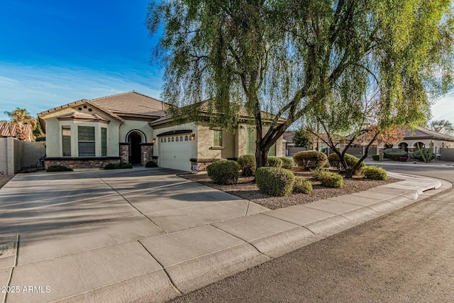 mediterranean / spanish-style home with a tiled roof, driveway, stone siding, an attached garage, and stucco siding