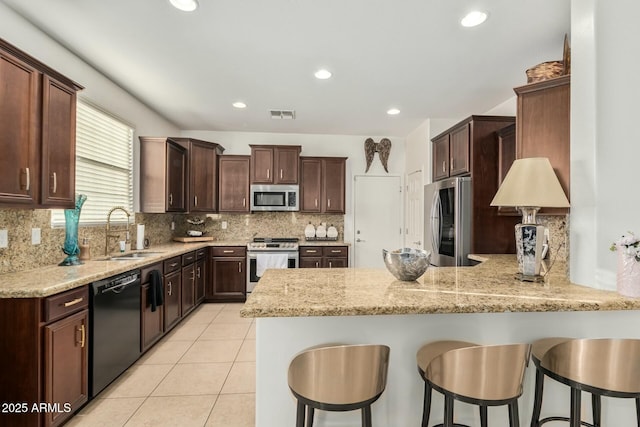kitchen featuring dark brown cabinets, visible vents, a sink, a peninsula, and appliances with stainless steel finishes