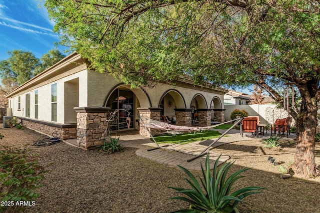 rear view of property with stucco siding, fence, a patio area, and stone siding