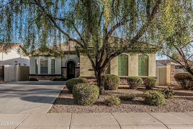 mediterranean / spanish house with concrete driveway, stone siding, a tiled roof, fence, and stucco siding