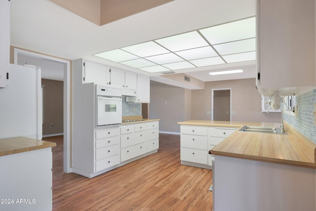 kitchen with sink, white oven, kitchen peninsula, white cabinets, and decorative backsplash