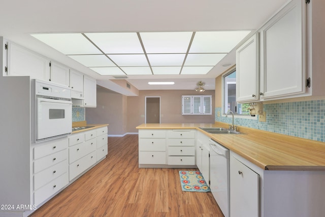 kitchen with kitchen peninsula, white cabinetry, light hardwood / wood-style floors, sink, and white appliances