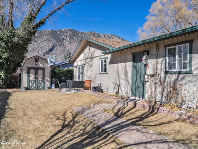 view of side of home featuring a mountain view, a patio area, a lawn, and a storage unit