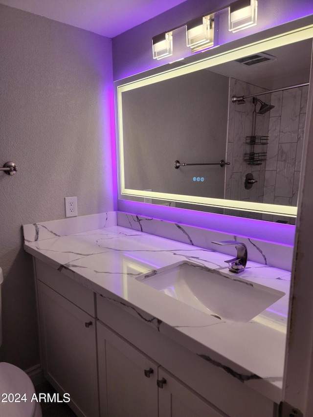 bathroom featuring toilet, vanity, and tiled shower