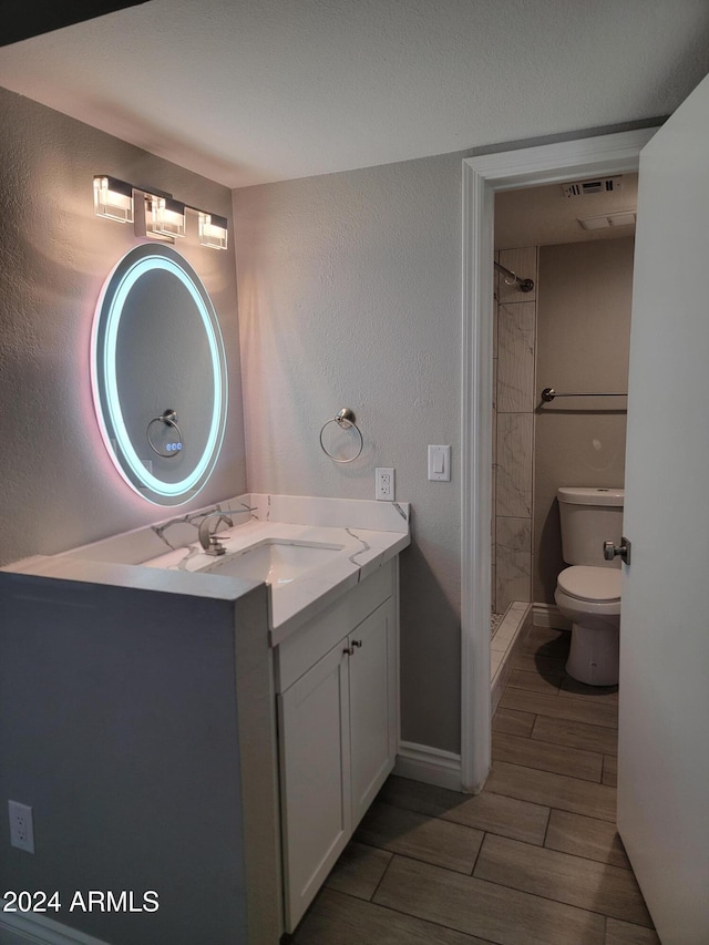 bathroom with a tile shower, hardwood / wood-style floors, vanity, and toilet