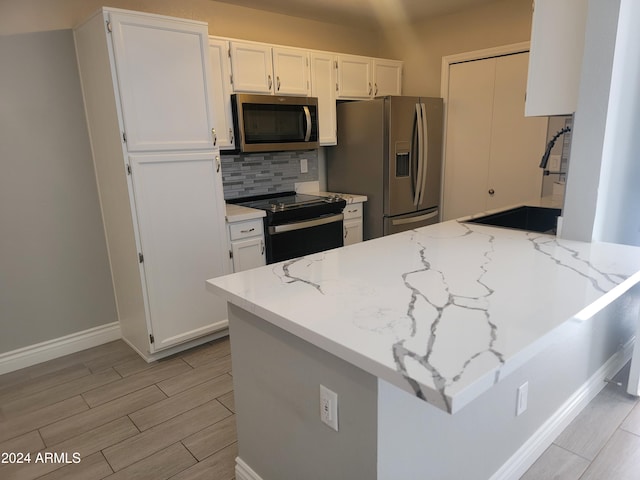 kitchen with decorative backsplash, stainless steel appliances, white cabinetry, and light stone counters