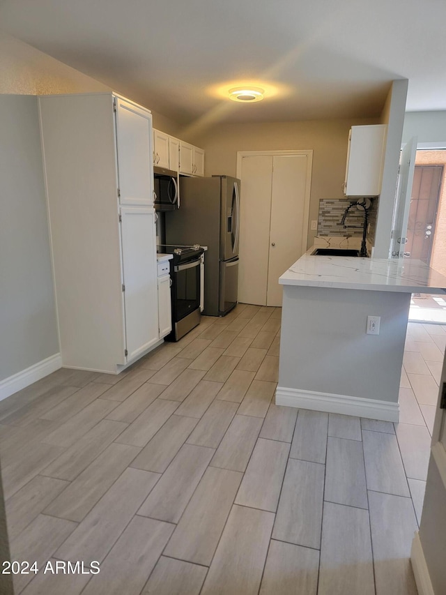 kitchen with kitchen peninsula, white cabinetry, sink, and appliances with stainless steel finishes